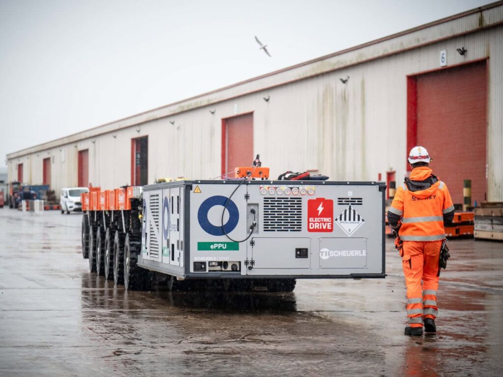 Selbstfahrender Scheuerle-Modultransporter mit elektrischer PowerPack Unit (ePPU), begleitet von einem Arbeiter im Hafeneinsatz