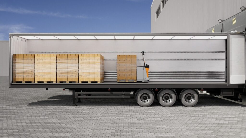 Sattelauflieger mit geöffneter Plane in der Seitenansicht, im Innern Paletten und ein autonomer Niederhubwagen STILL AXL 15 iGo