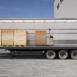 Sattelauflieger mit geöffneter Plane in der Seitenansicht, im Innern Paletten und ein autonomer Niederhubwagen STILL AXL 15 iGo