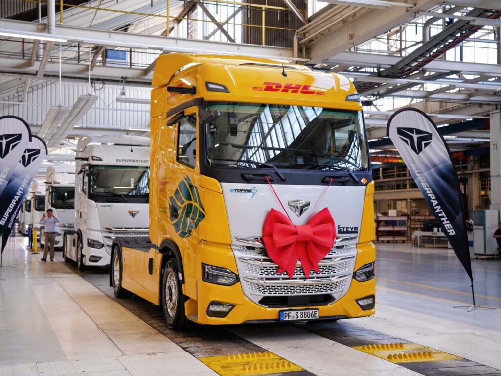 Eine Elektro-Sattelzugmaschine eTopas 600 von Superpanther am Ende der Fertigungsstraße von Steyr Automotive, lackiert im Design von DHL Freight und mit einer Schleife am Kühlergrill geschmückt