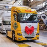 Eine Elektro-Sattelzugmaschine eTopas 600 von Superpanther am Ende der Fertigungsstraße von Steyr Automotive, lackiert im Design von DHL Freight und mit einer Schleife am Kühlergrill geschmückt