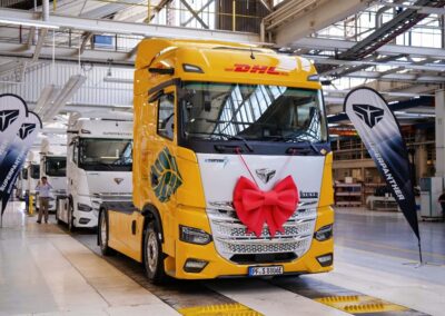 Eine Elektro-Sattelzugmaschine eTopas 600 von Superpanther am Ende der Fertigungsstraße von Steyr Automotive, lackiert im Design von DHL Freight und mit einer Schleife am Kühlergrill geschmückt