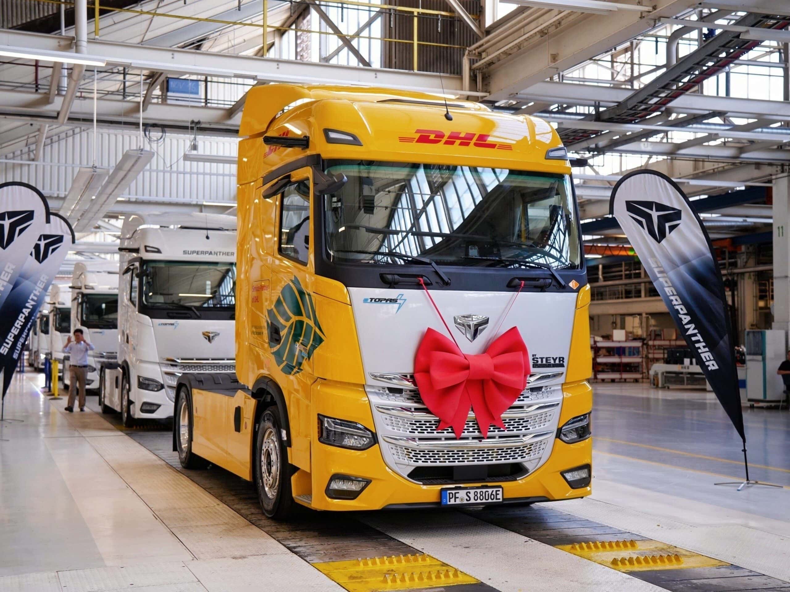 Eine Elektro-Sattelzugmaschine eTopas 600 von Superpanther am Ende der Fertigungsstraße von Steyr Automotive, lackiert im Design von DHL Freight und mit einer Schleife am Kühlergrill geschmückt