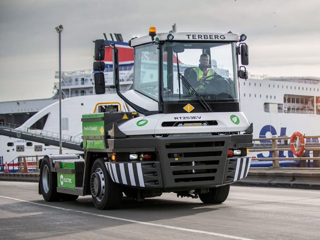 Batterieelektrischer Terminal-Traktor von Terberg, Typ RT253EV 4x4, solo auf einer Hafenstraße; im Hintergrund ein Fährschiff