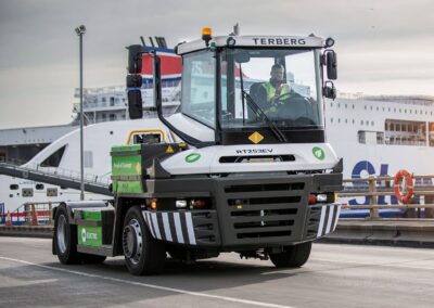 Batterieelektrischer Terminal-Traktor von Terberg, Typ RT253EV 4x4, solo auf einer Hafenstraße; im Hintergrund ein Fährschiff