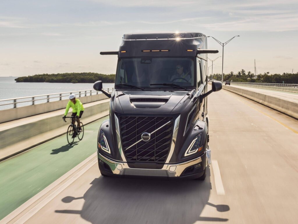 Nordamerikanischer Hauben-Lkw vom Typ Volvo VNR von vorn auf einer Straße, links daneben ein Radfahrer