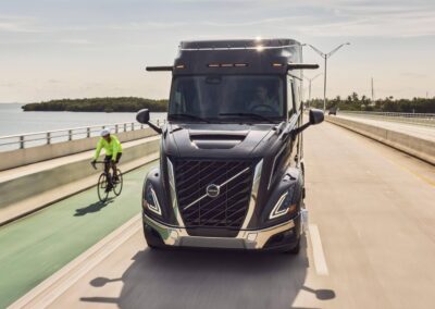Nordamerikanischer Hauben-Lkw vom Typ Volvo VNR von vorn auf einer Straße, links daneben ein Radfahrer
