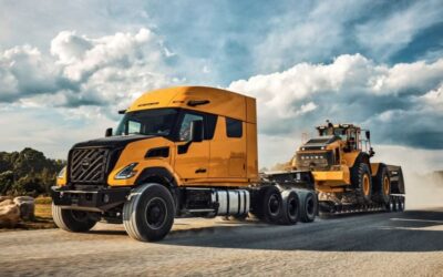Vierachsige Schwerlastzugmaschine vom Typ Volvo VNX 640, US-amerikanischer Hauber mit knapp 1,60 Meter langem Schlafabteil, im Einsatz auf staubiger Straße mit einem Volvo-Großradlader auf dem aufgesattelten Tiefbettauflieger