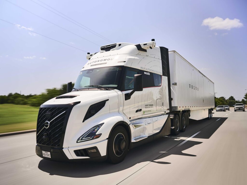 Autonom fahrender Sattelzug mit einer Hauben-Zugmaschine vom Typ Volvo VNL Autonomous mit virtuellem Fahrer „Waabi Driver“ auf einem Highway; fotografiert schräg von vorne, im Hintergrund fahren Pkw