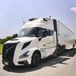 Autonom fahrender Sattelzug mit einer Hauben-Zugmaschine vom Typ Volvo VNL Autonomous mit virtuellem Fahrer „Waabi Driver“ auf einem Highway; fotografiert schräg von vorne, im Hintergrund fahren Pkw